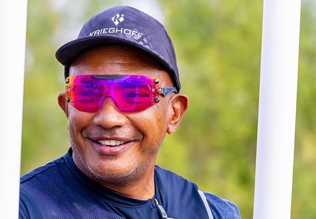 Shooter smiling on a sunny range day while wearing dark pink shooting glasses, illustrating how the right eyewear can support comfort, visibility, and safety.